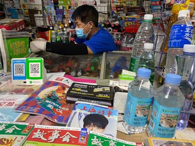 A news-stand vendor, wearing a mask to protect against the coronavirus, sits near QR codes for Alipay and WeChat, two popular online payment system in Beijing, China on July 21. AP