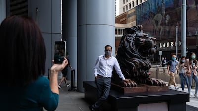 A person stands for a photograph next to a statue of a lion in front of the HSBC Holdings Plc headquarters building in Hong Kong. Bloomberg