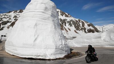 Walls of snow are seen beside as people ride on a bike during sunny weather on the St Gotthard mountain pass road, Switzerland. Reuters