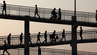 Pedestrians cross the E311 on a footbridge at sunset in Dubai. Chris Whiteoak / The National