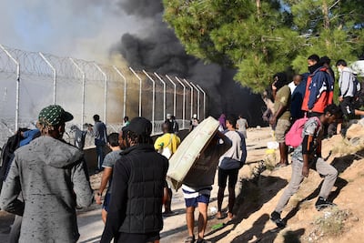 A migrant carries a mattress as others watch a fire inside a refugee camp on the eastern Aegean island of Samos, Greece, Wednesday, Nov. 11, 2020. Dozens of accommodations were destroyed by the fire that broke out on Wednesday morning, two weeks after an earthquake hit the island. (AP Photo/Michael Svarnias)