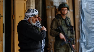 A Palestinian puts on a keffiyeh as an Israeli soldier stands guard in the old city in Hebron in the occupied West Bank, on February 9. Reuters