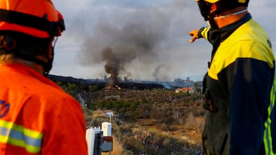 A member of La Palma's Civil Protection team and a firefighter watch as a house burns in the Cumbre Vieja National Park. Photo: Reuters