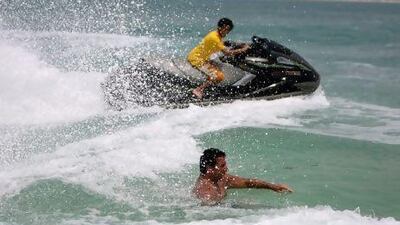 A jet skier rides his machine near a beach in Abu Dhabi very close to a man who is trying to swim, a situation which many say is a danger and should be illegal. Sammy Dallal / The National
