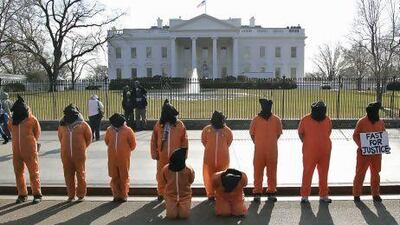 Human rights activists, hooded and wearing orange prison garb to represent prisoners at Guantanamo Bay, Cuba, protest in front of the White House because the prison has not been closed down by President Obama.