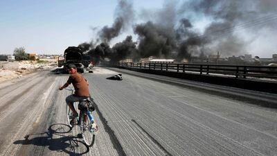 A Syrian boy rides a bicycle as smoke rises over Aleppo after missiles fired from a fighter jet hit petrol tankers. Youssef Boudlal / Reuters