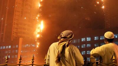 Residents watch as the fire spreads up the side of the building at Ajman One development. Many residents spent the night on the street after fleeing the burning tower block. Kamran Jebreili / AP Photo