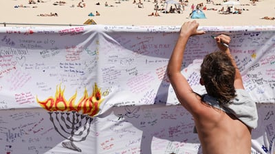 A mourner writes a message of a piece of cloth at the promenade of Bondi Beach in Sydney to honour victims of the shooting. AFP