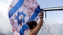 A woman holds an Israeli flag with red paint on to resemble blood as protesters block a main road during a rally in Tel Aviv. Getty
