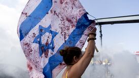 A woman holds an Israeli flag with red paint on to resemble blood as protesters block a main road during a rally in Tel Aviv. Getty