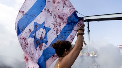 A woman holds an Israeli flag with red paint on to resemble blood as protesters block a main road during a rally in Tel Aviv. Getty