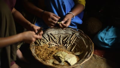 Women sit with a basket filled with tobacco flakes and cotton thread, materials used to roll bidis.
