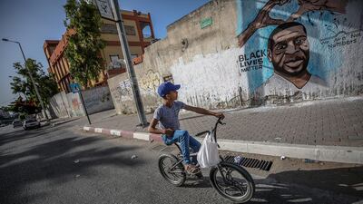 A Palestinian boy rides his bicycle next a mural of George Floyd in Gaza City. EPA