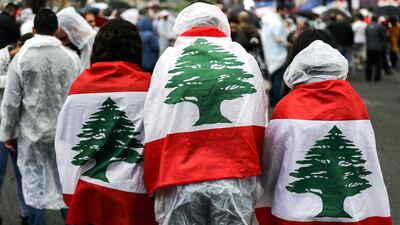 Protesters wearing ponchos and draped with the Lebanese national flag stand under the rain in Zouk Mosbeh, north of the capital Beirut. AFP