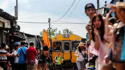 Tourists take photographs of a man running along rail tracks from a train traveling through the Maeklong Railway Market in Samut Songkram. Dario Pignatelli / Bloomberg News