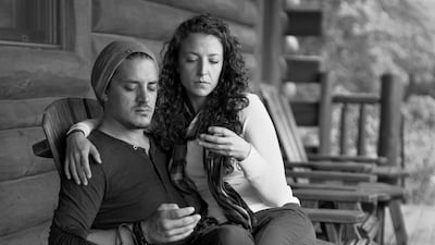 A woman sits on a man's lap on the porch of their house. Both are intently focused at the phones that should be in their hands. Courtesy Eric Pickersgill