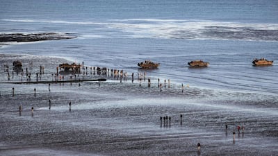 WWII enthusiasts walk near DUKW (colloquially known as Duck), a six-wheel-drive amphibious modification of the 2 1/2-ton CCKW trucks used by the US military, on the beach of Asnelles, in Normandy. APF