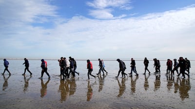 A group of people thought to be migrants walk along the beach after being brought to Dungeness in Kent on a RNLI Lifeboat. PA