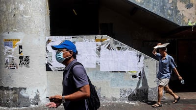 A man (R) walks past a wall with pro-democracy posters that have been covered over with blank paper in Hong Kong on July 3, 2020. AFP