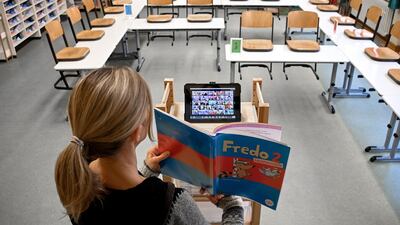 A teacher stands in an empty classroom and uses an iPad to teach children at home in Dinslaken, Germany. EPA