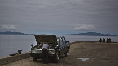A man repairs his car as others sit next to the sea Wonsan.