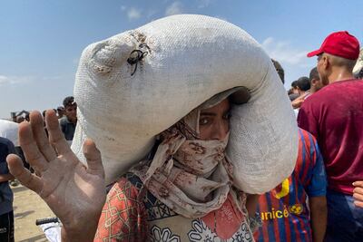 A woman carries a bag flour taken after displaced Palestinians raided trucks carrying humanitarian aid in Khan Yunis, in the southern Gaza Strip on August 9, 2025. AFP