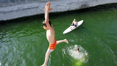 A boy jumps as Palestinian farmer Murad Abu Aram rides on a surfboard at his fish farm in a man-made pond in Hebron, in the Israeli-occupied West Bank. Reuters