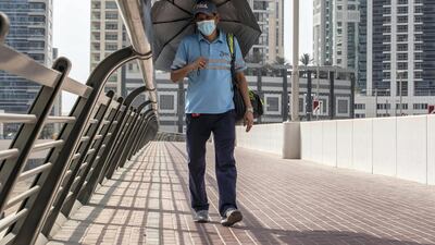 A man shields himself from the sun while walking across a bridge in Dubai Marina. Antonie Robertson / The National