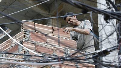 A man builds a wall on a favela building seen behind the mass of wires running along a street. The money spent on the Olympics in Rio are in stark contrast to the paralysed plans for improving the favelas' sanitation and services. Barbara Walton / EPA
