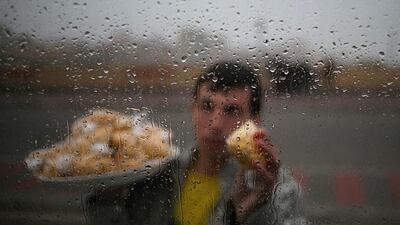 A Palestinian man selling packs of Lupini beans is seen from behind rain-covered glass near the Gaza City port on February 15, 2014. Mohammed Saber / EPA