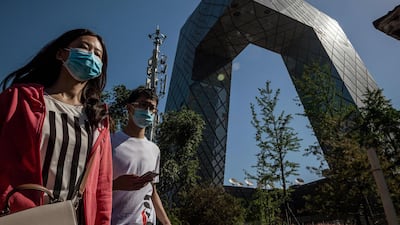 People wearing face masks walk past the CCTV building in Beijing on May 19, 2020. AFP