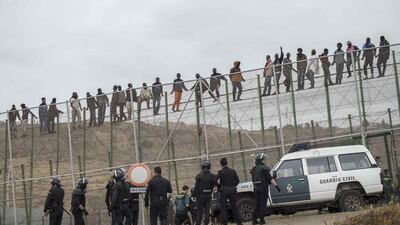 African migrants climb a border fence, as Spanish Civil Guard officers stand under them, during a latest attempt to cross into Spanish territory, between Morocco and Spain’s north African enclave of Melilla. Jesus Blasco de Avellaneda / Reuters