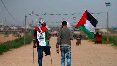 An amputee wearing a t-shirt depicting the colours of the Palestinian flag walks on crutches with another holding a Palestinian flag as they head towards a demonstration. AFP