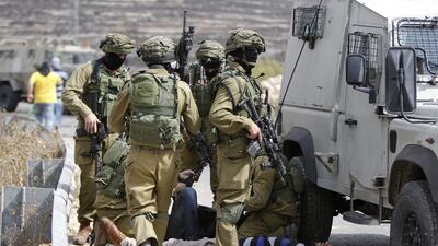 Israeli soldiers with their faces covered stand over Palestinians wounded during clashes in the West Bank on October 7, 2015. Majdi Mohammed / AP Photo