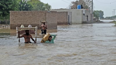 Flood affected people carry their belongings as they wade through flood water in Bahawalnagar of Punjab province on August 27, 2023. Families waded through water and cattle were loaded onto boats in a mass evacuation of around 100,000 people in Pakistan's Punjab province, officials said on August 23. (Photo by Shahid Saeed Mirza / AFP)