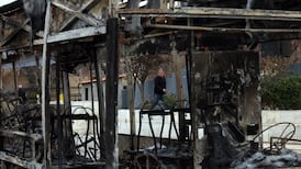Iranians walk near the wreckage of a burnt bus in Tehran. EPA