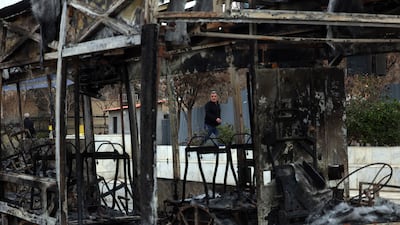 Iranians walk near the wreckage of a burnt bus in Tehran. EPA