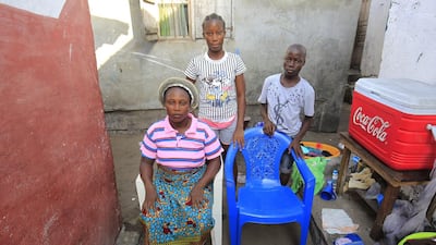 Siblings Comfort, left, Silvia, centre and Melvin Yeah pose for a family portrait at their home in Monrovia, Liberia. The empty chair symbolises their mother, who died of the Ebola virus disease during an outbreak of the disease in 2014. Ahmed Jallanzo / EPA