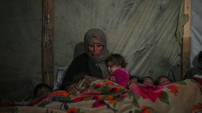 A Palestinian woman wraps herself and her grandchildren in blankets as they prepare to sleep in their tent at a camp in Khan Younis, Gaza. AP