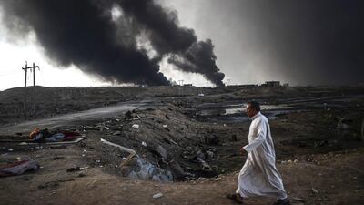 An Iraqi man walks as smoke rises behind him near Qayyarah. Bulent Kilic / AFP Photo