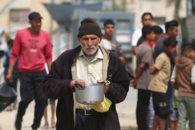 A displaced Palestinian man walks back to his family shelter with a pot of food collected from a charity kitchen in the Bureij refugee camp in the central Gaza Strip on May 18, 2026. AFP