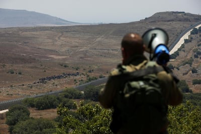 An Israeli soldier speaks over a megaphone to people standing next to the border fence between Israel and Syria. Reuters
