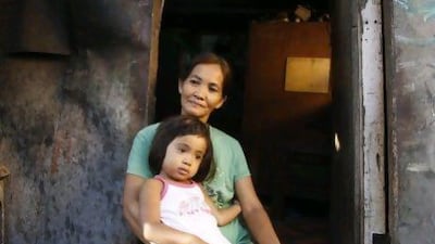 Fe Capco, a beneficiary of government's Conditional Cash Transfer programme holds her daughter Rihanna on her lap at the entrance of their shanty in Pateros in Metro Manila.
