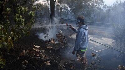 A resident hoses smouldering logs as a bushfire burns in Woodford, New South Wales (NSW), Australia. EPA