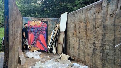 Jared Whipple stands next to a painting by Francis Hines found in a dumpster, Sept. 23, 2017, in Watertown, Conn. After fading into obscurity, Hines, who died in 2016, is again gaining attention after hundreds of his paintings were rescued by a car mechanic from a dumpster in Connecticut. An exhibit of that art will open May 5, 2022, at the Hollis Taggart galley in Southport, which is known for showing the works of lost or forgotten artists. (Scott Whipple via AP)