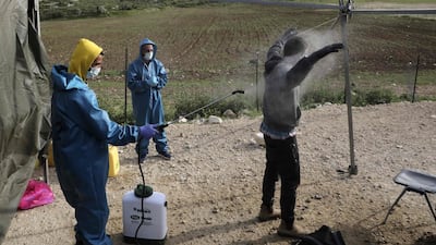 An employee at the Palestinian ministry of health sprays disinfectant on a worker returning from Israel through the Tarqumiah crossing, north-west of the West Bank city Hebron to stem the spread of the COVID-19 pandemic. AFP