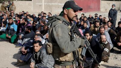Men sit on the ground as an Iraqi Special forces intelligence team check their ID cards as they search for ISIL fighters.