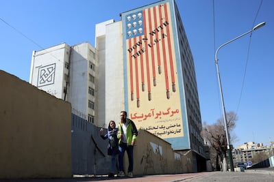 An Iranian couple walk past an anti-US mural on a building in Tehran on February 26, 2026. A third round of indirect talks between the United States and Iran, mediated by Oman's foreign minister, opened in Geneva on February 26 morning, a diplomatic source told AFP. (Photo by AFP)