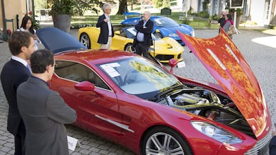 People look at a Aston Martin One-77 Coupe (2011) in front of a Ferrari LaFerrari (2015), yellow, and a Bugatti Veyron EB 16.4 Coupe (2010). The Aston went for 1.55 million francs. EPA