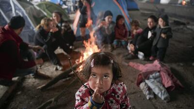 A child eats as other migrants sit around a fire in a railway repairs hangar at Idomeni on the Greece-Macedonia border on March 18, 2016. Vadim Ghirda / AP Photo